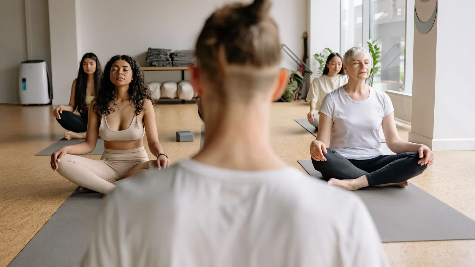 Ein Lehrer leitet eine Gruppe in sitzender Meditation in einem hellen Yogastudio an